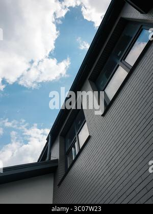 Windows under the roof on last floor of the building. Looking up at the grey brick building and clear blue sky in the background. Stock Photo