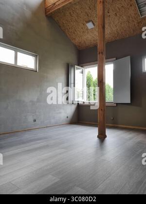 Modern interior - industrial-rustic design blend with exposed wood beams, soaring ceiling, concrete walls, dark hardwood floors and several windows. Stock Photo