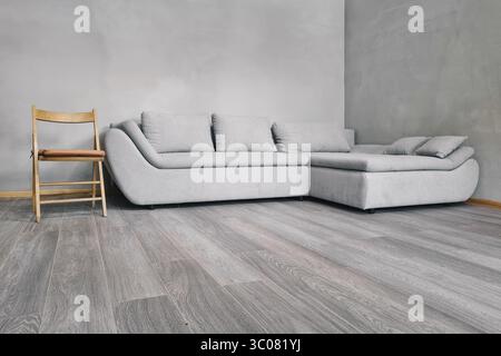 Interior design scene with a sofa and a chair. Wooden fold chair and light grey sofa in a room with concrete walls and grey wooden floor. Stock Photo