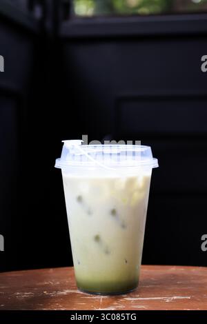 Iced Matcha Latte Green Tea with Milk Foam in a Plastic Takeaway Glass on a Wooden Table. Stock Photo