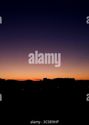 Dusk over the city. Glowing sunset sky gradient over urban skyline - gradient from glowing orange to purple. Stock Photo