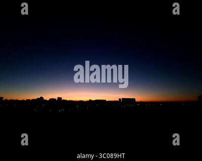 Dusk over the city. Glowing sunset sky gradient over urban skyline - gradient from glowing orange to dark blue. Stock Photo