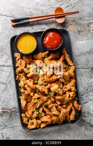 Chinese fast food crispy small pork xiaosurou with sauces close-up on plate on table. Vertical top view from above Stock Photo