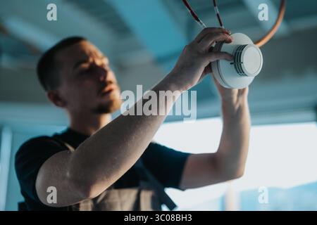 Technician installing a ceiling-mounted smoke detector device in a modern setting. Stock Photo