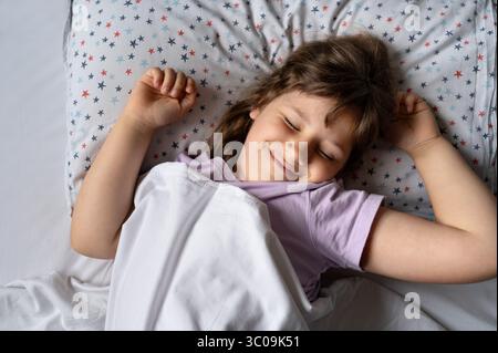 Child girl stretching in bed with a big smile. Stock Photo