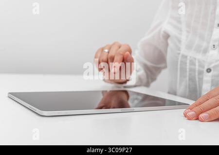 A person in a white shirt interacts with a tablet. Stock Photo