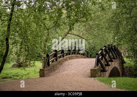 A curved stone bridge with a wooden railing in green park. Stock Photo