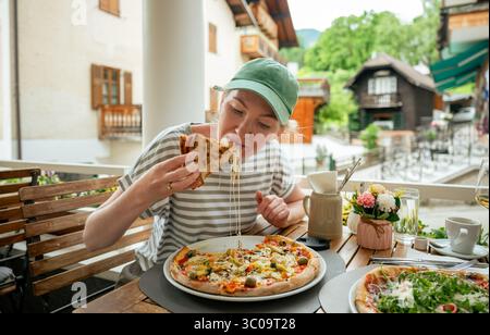 Woman eating pizza at outdoor cafe in scenic Austrian village Stock Photo
