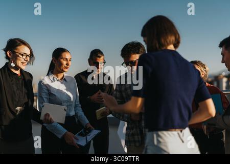 A diverse group of business people relax and socialize on a high-rise balcony at sunset, enjoying music and conversation. Stock Photo