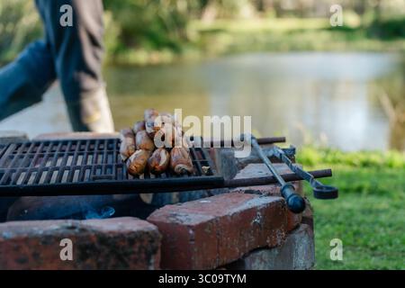 Grilling sausages over open fire at lakeside brick fire pit Stock Photo