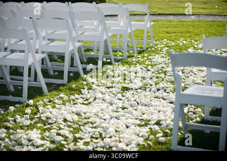 White chairs and flower petal aisle set up for outdoor ceremony Stock Photo