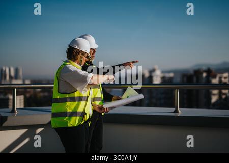 Architects discussing construction plans on a rooftop with urban skyline Stock Photo