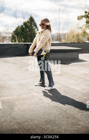 Stylish woman holding skateboard while standing on roof Stock Photo