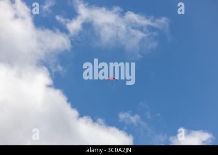 View of a lone paraglider suspended against the vibrant blue canvas dotted with soft, fluffy clouds, Oderen, Grand Est, France. Stock Photo