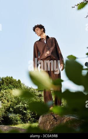 Curly-haired young man showcases a trendy summer outfit while exploring a beautiful park. Stock Photo