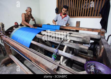Two workers do the spinning process of the basic material for woven fabrics in a factory that still uses traditional equipment. Stock Photo