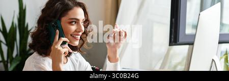 Young woman with curly hair talks cheerfully on the phone while focusing on her work at home, banner Stock Photo