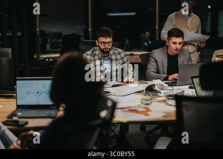 Diverse group of colleagues brainstorms and collaborates during a late-night business meeting. Stock Photo