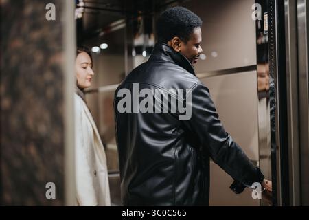 Two people using an elevator with a sleek interior, one pressing a button, showcasing modern transportation and urban lifestyles. Stock Photo