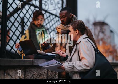 Multiracial people collaborating outdoors with a laptop and documents Stock Photo