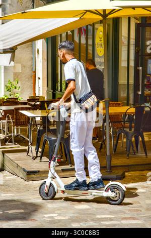 Young Oriental male on electric scooter in town center - Loches, Indre-et-Loire (37), France. Stock Photo