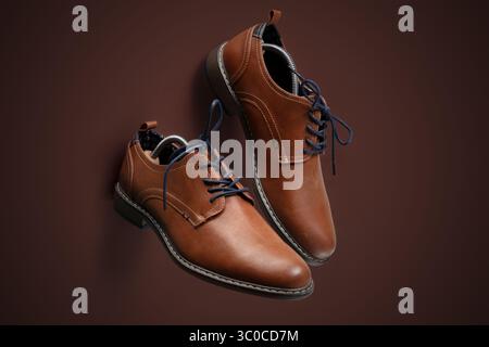 Pair of stylish brown leather dress shoes with black soles and dark laces, presented on a matching brown background. Classic footwear ideal for formal Stock Photo