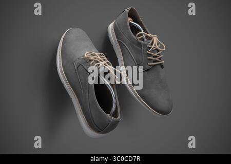 Top view of a pair of modern gray suede casual shoes with beige laces and white soles, arranged diagonally on a smooth gray background. Shoe trees are Stock Photo