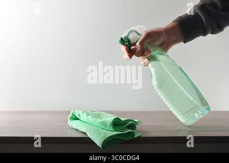 Hand with a product for home cleaning applying on a wooden piece of furniture with a green microfiber cloth and white isolated background. Front view. Stock Photo