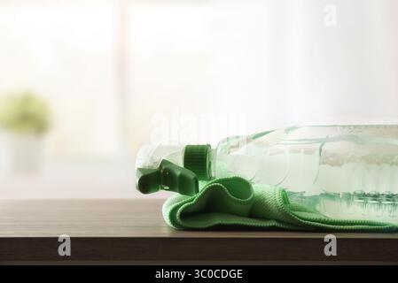 Cleaning product for dirt and dust in a transparent plastic bottle spray on wooden table with green microfibre cloth with room in the background. Fron Stock Photo