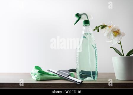 Window cleaner spatula, spray product, microfibre cloth and plant on wooden table isolated background. Front view. Stock Photo