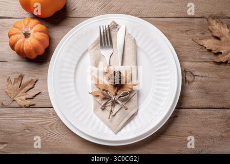 Thanksgiving Day or Halloween  place setting with pumpkins and dry maple leaves on wooden background, top view. Neutral autumn holiday table setting. Stock Photo