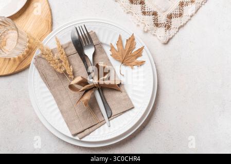 Autumn elegant place setting with dry maple leaves and linen napkins on white background, top view, copy space. White autumn boho style Thanksgiving t Stock Photo