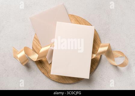 Blank card 5x7 and envelope mockup with golden silk ribbon, space for text, design template. Beige wedding invitation card design. Stock Photo