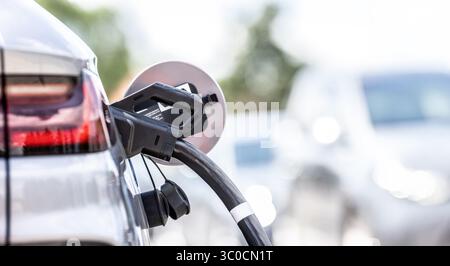 Focus closeup electric vehicle plugged in with EV charger device from blurred background of public charging station powered by renewable clean energy Stock Photo