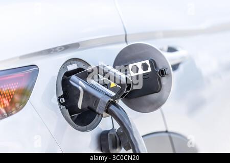 Focus closeup electric vehicle plugged in with EV charger device from blurred background of public charging station powered by renewable clean energy Stock Photo