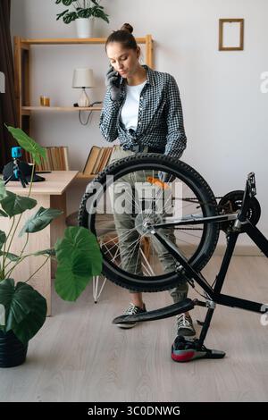 Woman talking on cellphone with technician or repairman while fixing broken bike at home Stock Photo