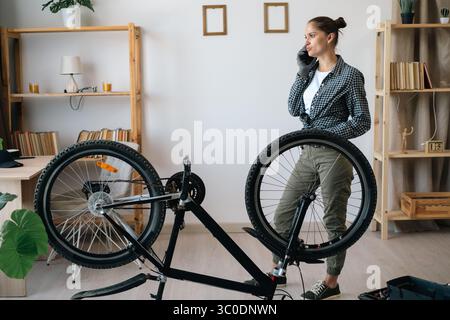 Woman talking on cellphone with technician or repairman while fixing broken bike at home Stock Photo
