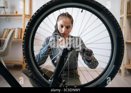 Young woman talking on mobile phone with mechanic asking for advice on servicing repairing broken bicycle Stock Photo