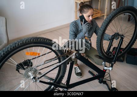 Woman talking on cellphone with technician or repairman while fixing broken bike at home Stock Photo