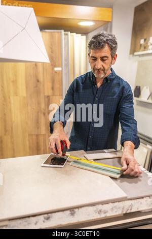 Architect taking measurements of ceramic tile using a tape measure and tablet in a home improvement store showroom Stock Photo