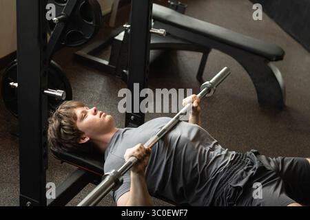 High angle view of young caucasian man doing bench press exercise with barbell in modern gym. Warming up. Chest workout Stock Photo