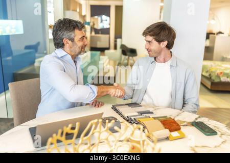 Interior designer shaking hands with a client in a furniture store showroom after choosing upholstery and fabric swatches Stock Photo