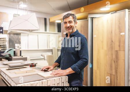 Smiling architect choosing material samples in a home improvement store, he is touching ceramic and wood tiles Stock Photo