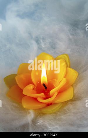 Yellow lotus flower candle burning with small flame, floating on white clouds with blue sky background Stock Photo