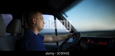 A man focused on driving, illuminated by a sunset Stock Photo