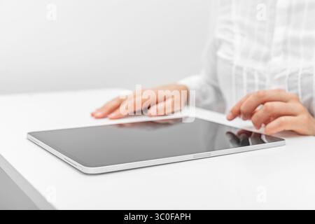 A person in a white shirt interacts with a tablet. Stock Photo