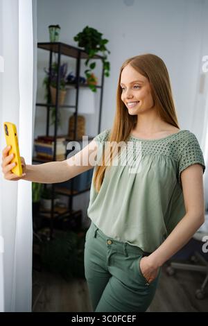 Smiling woman takes a selfie in a cozy indoor setting with plants Stock Photo
