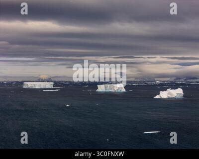 Aerial view of the stark white icebergs drift on the dark, brooding sea under a heavy, clouded sky, Seymour Island, Antarctica. Stock Photo