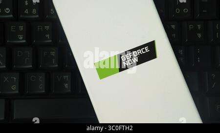 Smartphone displaying 'GEFORCE NOW' logo on white background, black keyboard visible Stock Photo