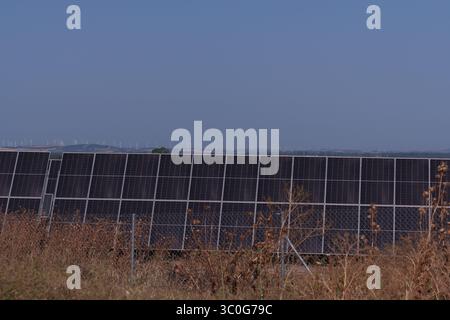 Renewable energy infrastructure showing solar panels generating electricity, wind turbines spinning against blue sky background Stock Photo